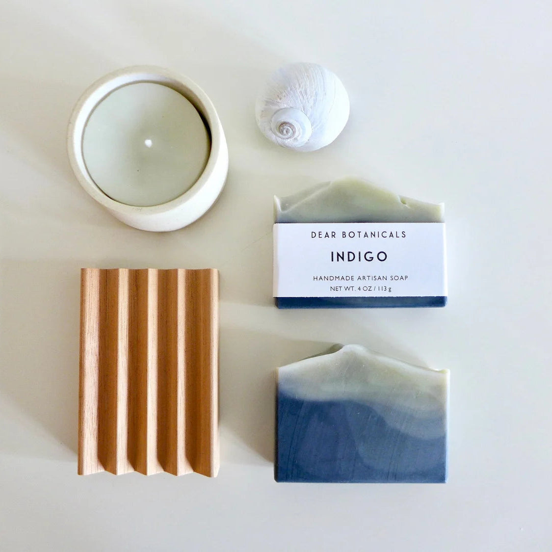 Two bars of soap and a candle on a white surface with 'Dear Botanicals' packaging.